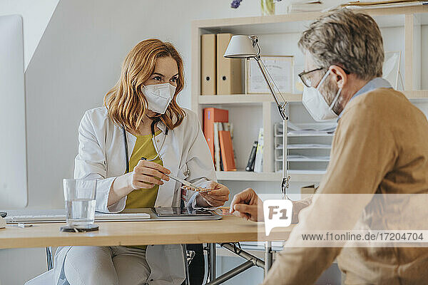 Arzt mit Gesichtsschutzmaske bei der Erläuterung von Medikamenten in einer Arztpraxis