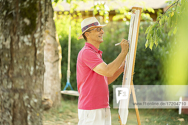 Glücklicher älterer Mann  der im Garten auf einer Leinwand zeichnet
