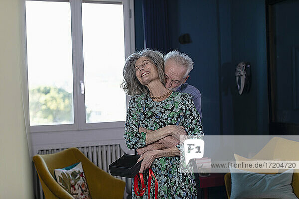 Älterer Mann umarmt lächelnde Frau  während er zu Hause steht