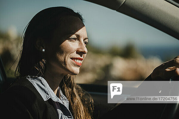 Geschäftsfrau lächelnd beim Autofahren an einem sonnigen Tag