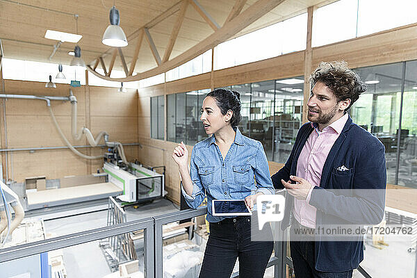 Businesswoman holding digital tablet while looking away with male colleague in factory