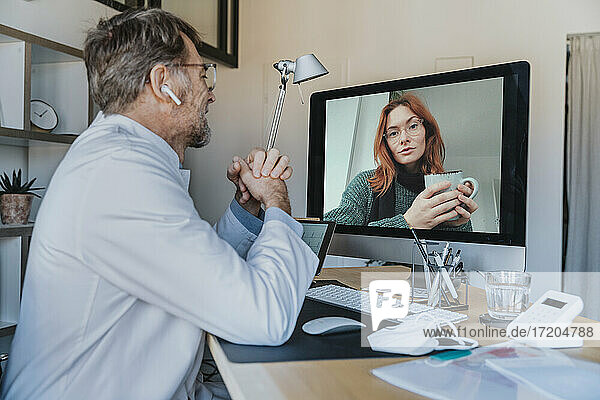 Männlicher Arzt im Gespräch mit einem Patienten über Computer per Videoanruf in einer Klinik