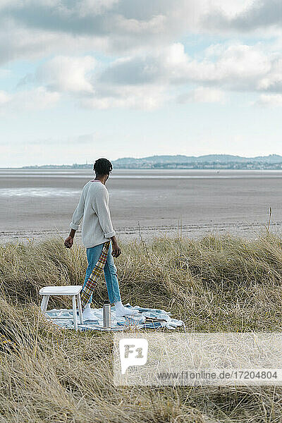 Mann schaut in die Ferne  während er inmitten von getrockneten Pflanzen am Strand vor bewölktem Himmel steht