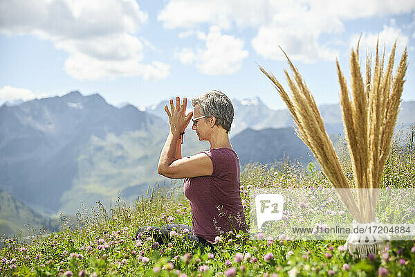 Active woman with hands clasped meditating amidst plants against sky