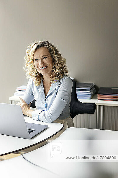 Lächelnde Geschäftsfrau mit Laptop am Schreibtisch sitzend im Büro