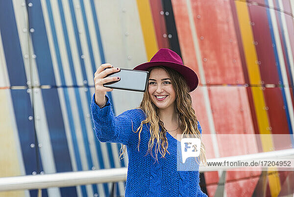 Junge Frau  die ein Selfie mit ihrem Smartphone vor einer bunten Wand macht