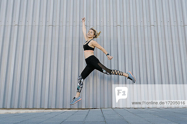 Carefree female athlete jumping by wall during sports training