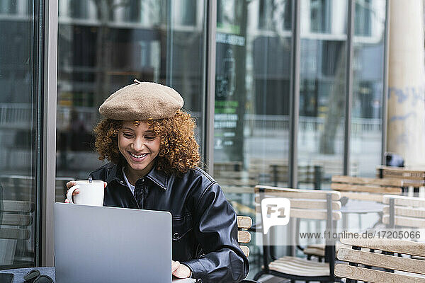 Weiblicher Teenager mit Kaffeetasse und Laptop in einem Straßencafé
