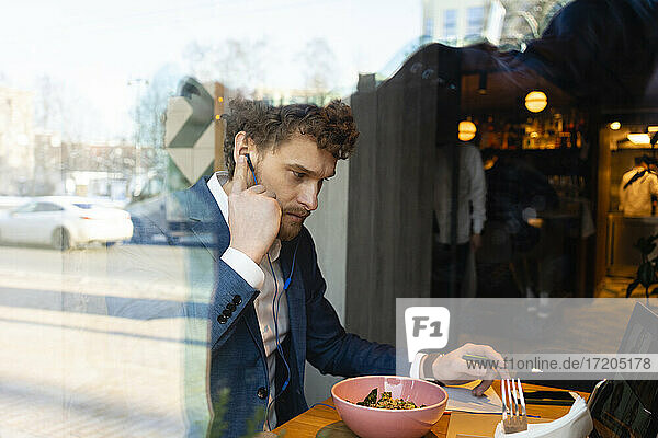 Verwirrter Geschäftsmann spricht während eines Videoanrufs  während er in einem Café isst