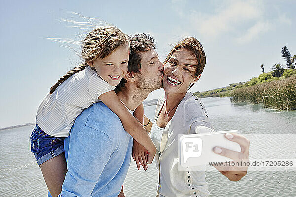Fröhliche Familie nimmt Selfie durch Handy am See