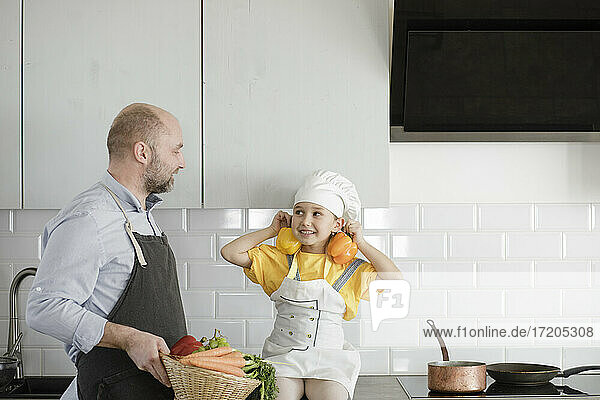 Lächelnde Tochter spielt mit Gemüse  während sie neben ihrem Vater in der Küche steht