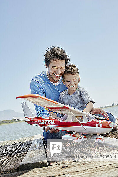 Lächelnder Vater und Sohn spielen mit Flugzeugspielzeug auf dem Steg