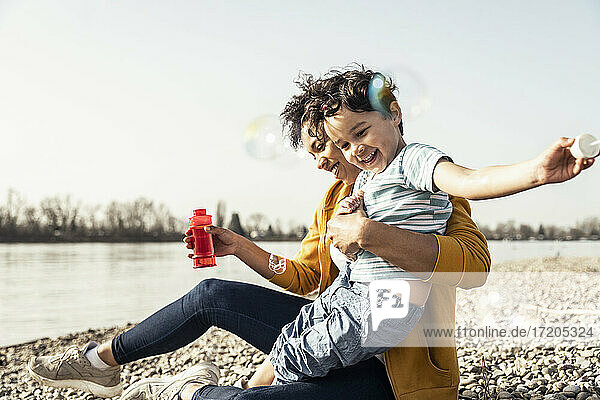 Playful mother and son playing with bubble soap on sunny day