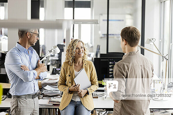 Lächelnde Unternehmerin mit Laptop  die mit Kollegen am Schreibtisch im Büro diskutiert