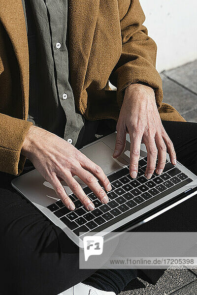 Businessman wearing jacket working on laptop while sitting outdoors