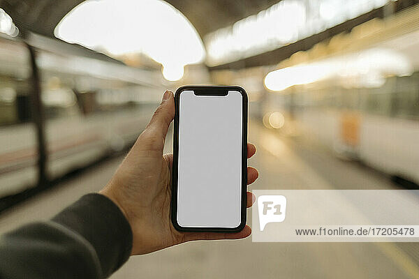 Junger Mann benutzt Telefon mit leerem Bildschirm am Bahnhof