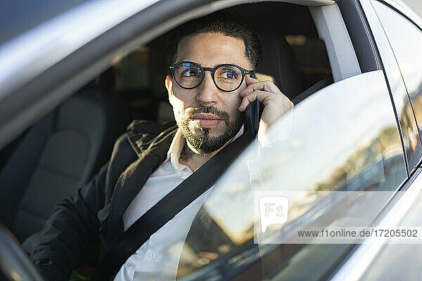 Gutaussehender Geschäftsmann schaut weg  während er im Auto mit seinem Handy telefoniert