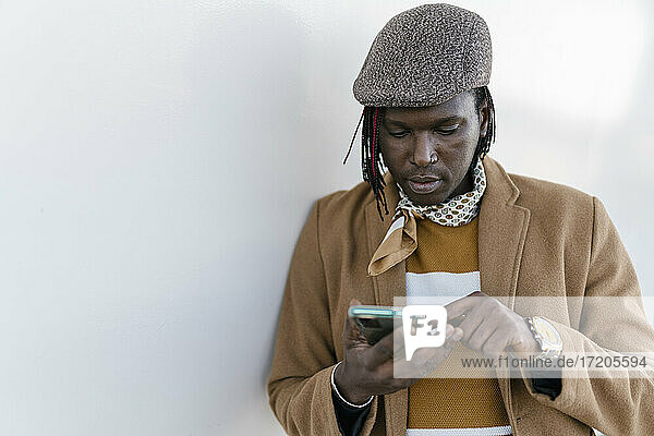 Afrikanischer Mann benutzt ein Smartphone an einer weißen Wand