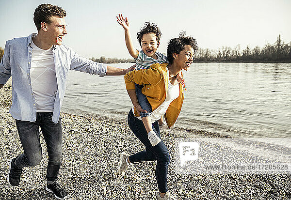 Fröhliche Familie hat Spaß beim Laufen am Seeufer an einem sonnigen Tag