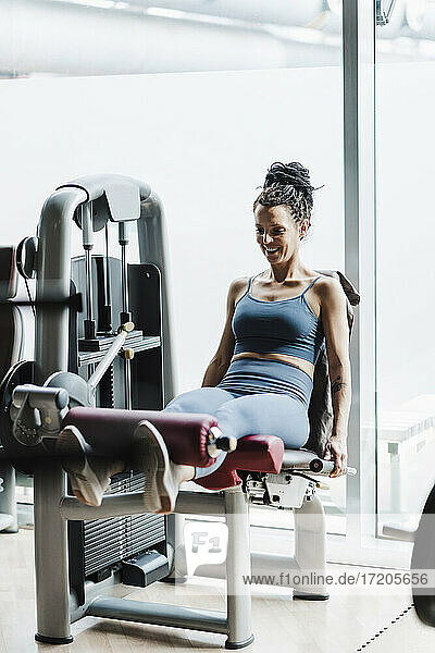 Lächelnde Sportlerin  die im Fitnessstudio an einer Gewichthebevorrichtung trainiert