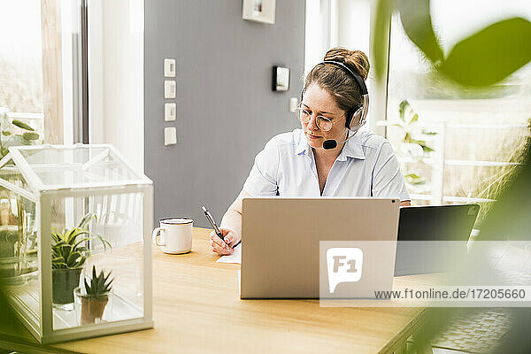 Unternehmerin mit drahtlosen Kopfhörern bei der Arbeit an einem Dokument am Schreibtisch