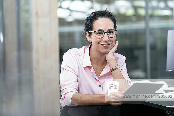 Lächelnde Geschäftsfrau mit Brille hält digitales Tablet im Büro