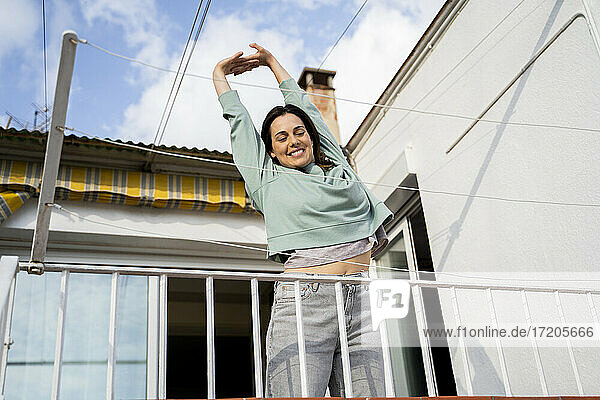 Smiling woman stretching hand while standing at balcony