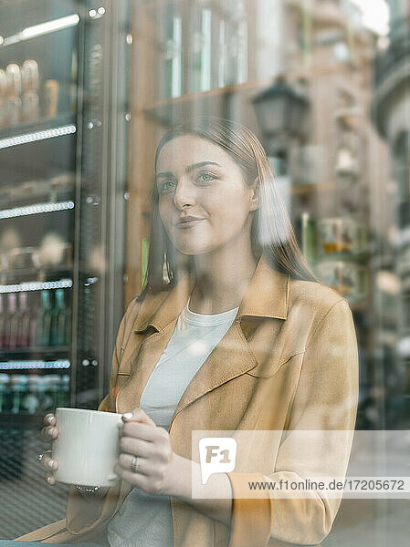 Lächelnde junge Frau schaut durch das Fenster eines Cafés
