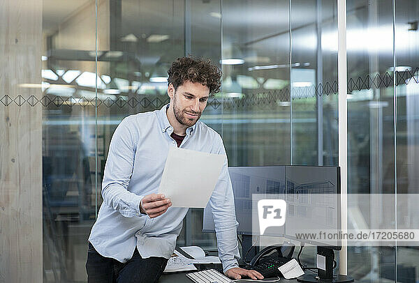 Male entrepreneur looking at strategy while leaning on desk at factory