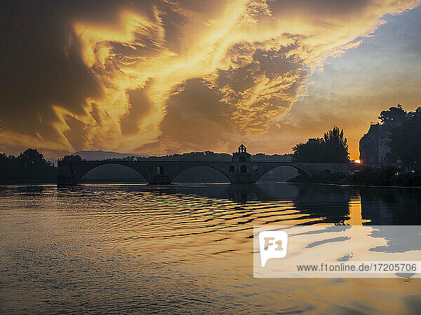 Clouds over river Rhone at sunset with silhouette of arch bridge in background  Vaucluse  France