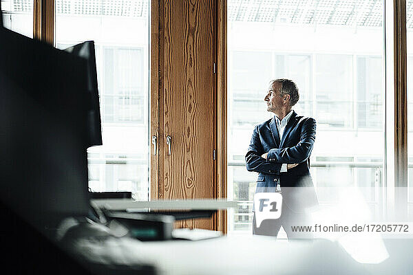 Contemplating male entrepreneur looking through window while standing against window