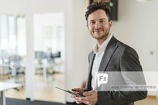 Smiling handsome businessman with digital tablet in office