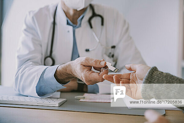 Ein Arzt gibt einem Patienten einen USB-Stick  während er am Tisch in der Arztpraxis sitzt