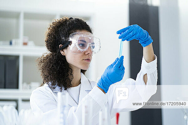 Junge Wissenschaftlerin  die ein Reagenzglas im Chemielabor untersucht