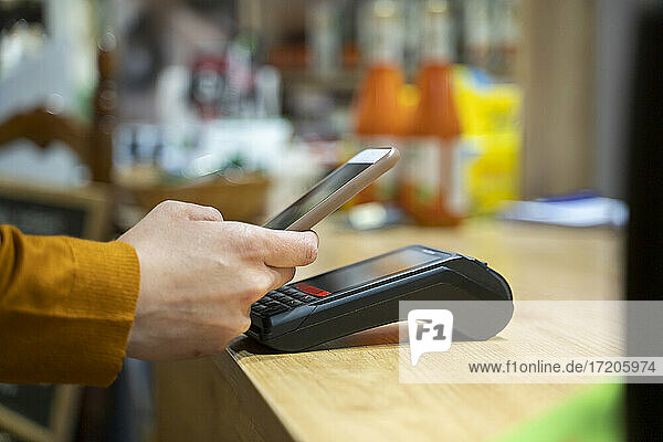 Frau benutzt Smartphone zum kontaktlosen Bezahlen an der Kasse eines Lebensmittelgeschäfts