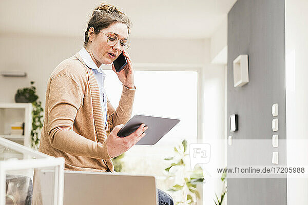Female professional holding digital tablet while talking on mobile phone