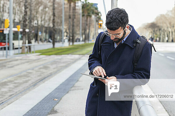 Männlicher Geschäftsmann  der ein digitales Tablet benutzt und sich am Geländer eines Bahnhofs anlehnt