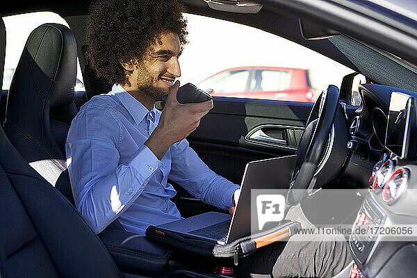Male professional holding smart phone while using laptop in car
