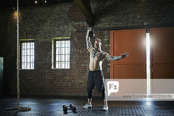 Hemdloser männlicher Athlet  der eine Kettlebell hebt  während er im Fitnessstudio trainiert