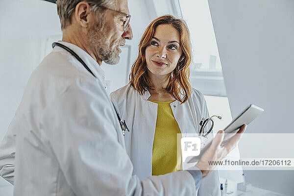 Mitarbeiterin betrachtet Arzt bei der Verwendung eines digitalen Tablets in der Klinik