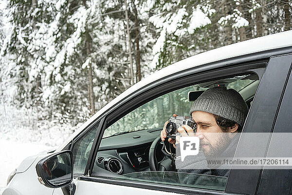 Young man photographing through camera while sitting in car