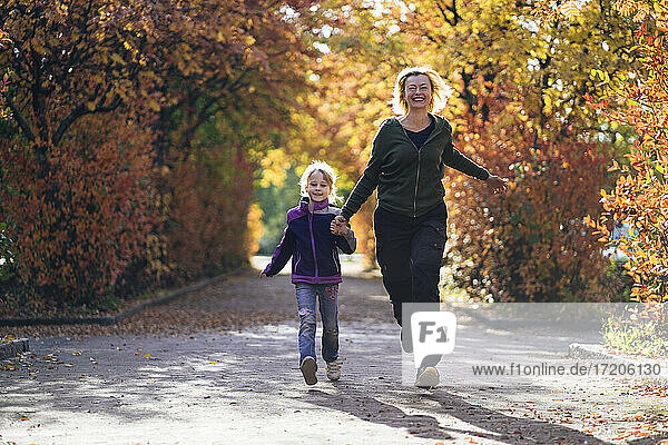 Glückliche Mutter und Tochter halten sich an den Händen und laufen im Herbst im Park