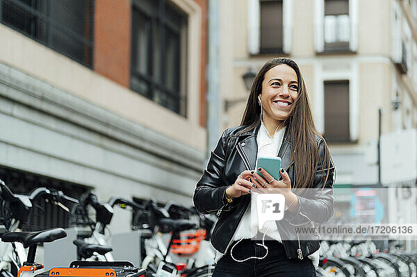 Lächelnde Frau hört Musik durch Smartphone auf der Straße in der Stadt