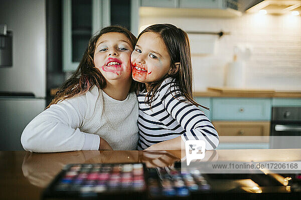 Mädchen mit Make-up im Gesicht umarmen sich gegenseitig  während sie am Esstisch sitzen