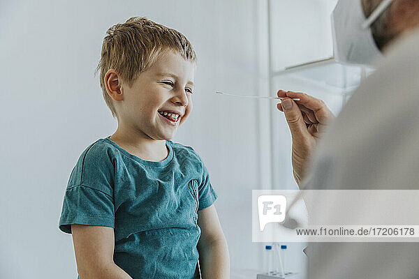 Lächelnder Junge bei einem Nasenabstrich  der von einem Arzt in einer Klinik durchgeführt wird