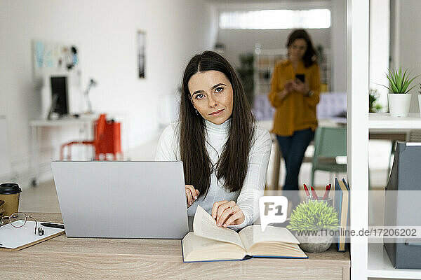 Junge Frau mit Laptop sitzt am Tisch im Wohnzimmer