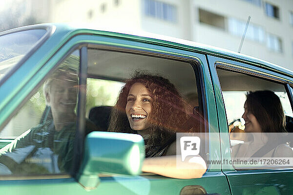 Smiling woman looking away while sitting with friends in car