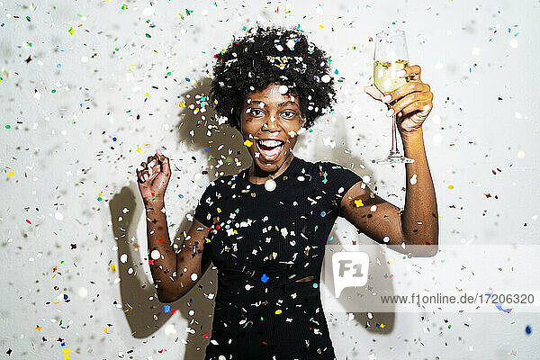 Glückliche Frau mit Champagnerflöte tanzen  während stehend inmitten von Konfetti gegen weißen Hintergrund