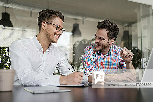 Glückliche männliche Unternehmer mit Laptop auf dem Schreibtisch im Büro