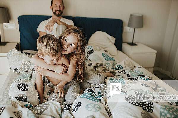Vater beobachtet Mädchen und Jungen beim Spielen im Bett